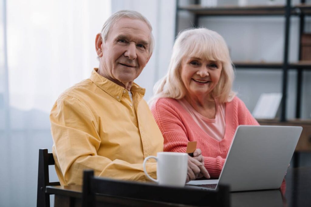 happy retired couple sitting at desk with laptop